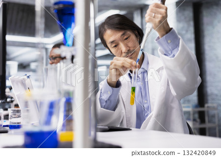 Senior molecular biologist conducting pipetting operation for sample preparation in controlled laboratory environment. Asian research facility professional using pipette for liquid measurement Senior molecular biologist conducting pipetting operation for sample preparation in controlled laboratory environment. Asian research facility professional using pipette for liquid measurement 132420849