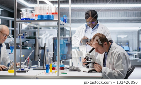Team of experts investigate molecular samples at microscope with laboratory tray and lens system, magnification tools support diagnostics and biotechnology breakthrough in science. Team of experts investigate molecular samples at microscope with laboratory tray and lens system, magnification tools support diagnostics and biotechnology breakthrough in science. 132420856