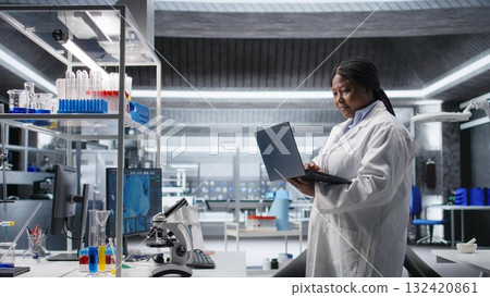 Black female researcher in a clinical research lab studies experiment data with a laptop. Showcasing biotechnology, genetics research and pharmacology for progress in healthcare. 132420861