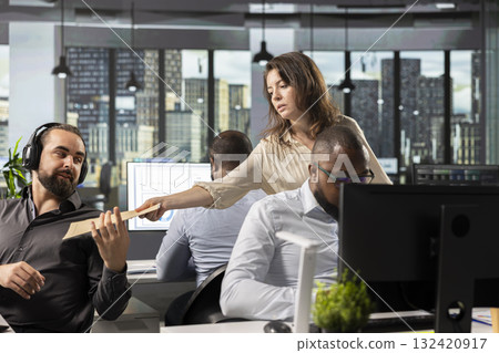 Workplace support person offers documents to colleagues in office, carrying archived files and folders with a moving cart. Assisting in task completion and business intel, projections. 132420917