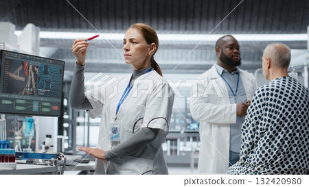 Female doctor checks blood samples from patient during clinical trial, monitoring vitals, dosage reactions and treatment progress. Woman works on advancing healthcare science. Camera B. Female doctor checks blood samples from patient during clinical trial, monitoring vitals, dosage reactions and treatment progress. Woman works on advancing healthcare science. Camera B. 132420980