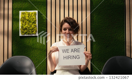 Human resources employee displaying signs for recruiting as part of advertising campaign to attract professional candidates to available positions within business. Talent retention. Camera A. Human resources employee displaying signs for recruiting as part of advertising campaign to attract professional candidates to available positions within business. Talent retention. Camera A. 132421067