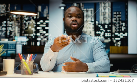 Black male CEO meeting with investors group on teleconference call, attending a remote discussion via telephone line from office desk. Employee networking, negotiating with board members. 132421107