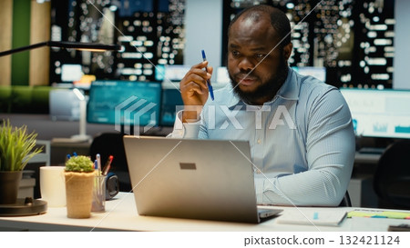 Black general manager envisioning a tactical solution and playing with pen, working late alone in office. Guy engaging in critical thinking, evaluating options and solutions for dilemma. Black general manager envisioning a tactical solution and playing with pen, working late alone in office. Guy engaging in critical thinking, evaluating options and solutions for dilemma. 132421124