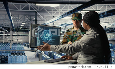 Military staff in server room uses AI tools to help manage computer systems. Army team wearing uniform reviews information using artificial intelligence programs in server farm, camera A 132421127