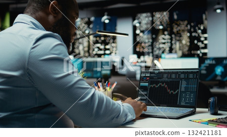 African american consultant examining data on stock and forex trading, preparing reports and forecasts that drive business development. Building a modern investment strategy at night. African american consultant examining data on stock and forex trading, preparing reports and forecasts that drive business development. Building a modern investment strategy at night. 132421181