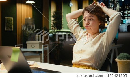 Businesswoman struggling to stay awake after an intense workload, lounges across desk at midnight. Fatigue, mental haze and workplace challenges have left her drained and restless. Camera A. 132421205