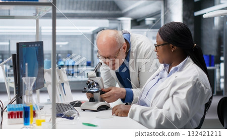 Researcher using microscope and specimen tray in laboratory workspace. Optical instrument, lens system and magnifying glass support clinical testing and biotechnology for healthcare. 132421211