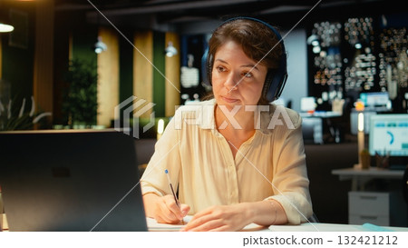 Woman joining a remote webinar from desk using laptop and headset, interacting with participants. Person maintaining eye contact, exchanging ideas in a chat that promotes networking. Camera A. 132421212