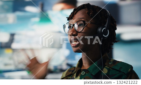 Close up of army telecommunications operator uses tablet and headset to manage secure military communications. Soldier coordinates mission support from command center with surveillance technology 132421222