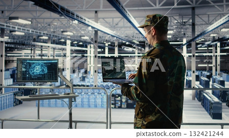 Military engineer in data center tracking satellite coordinates using laptop interface. Soldier in server room analyzing reconnaissance data through satellite imaging systems, camera A Military engineer in data center tracking satellite coordinates using laptop interface. Soldier in server room analyzing reconnaissance data through satellite imaging systems, camera A 132421244