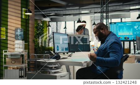 Black male administrator in modern workspace analyzing forecast insights and business strategy on a computer monitor, ensures report writing and planning for productivity. 132421248