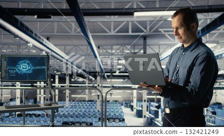 Data center IT professional deploys deep learning software on infrastructure racks. Server farm engineer trains AI systems with datasets using laptop to support applications, camera A 132421249