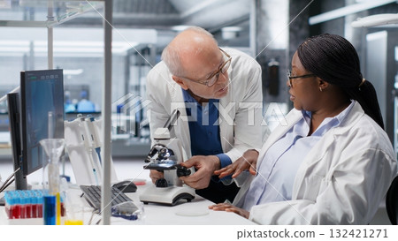 African American scientist focuses on a microscope with tray of samples in modern laboratory. Using observation tool for diagnostics, molecular analysis and discovery. Optics in bioscience. 132421271