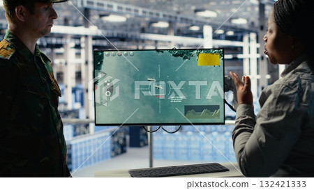 Military data center coworkers looking at radar software on screen to watch for enemy threats. Team of army employees in data center scans suspicious activity to detect dangers, camera B Military data center coworkers looking at radar software on screen to watch for enemy threats. Team of army employees in data center scans suspicious activity to detect dangers, camera B 132421333