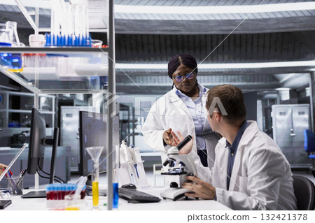 Diverse experts examining microscope slide with laboratory tray. Magnified molecular analysis and pathology research demonstrate innovation in diagnostics, biochemistry and science. 132421378