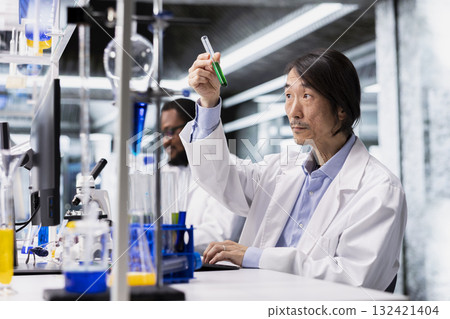 Senior laboratory chemist inspects clarity of chemical solution in vial for purity verification. Biochemist at work prepares reagent vials for assay procedures during clinical trials 132421404