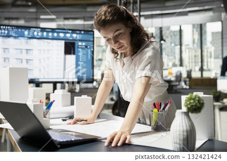 Female contractor prepares construction blueprints by reviewing urban models and structural designs for a modern apartment construction project. Property search documents and investment plans. Female contractor prepares construction blueprints by reviewing urban models and structural designs for a modern apartment construction project. Property search documents and investment plans. 132421424