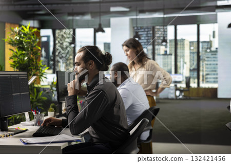 Male professional in a corporate workspace coordinates tasks and objectives. Employee reviews files, projections and business intel to drive progress and resource allocation for company. 132421456