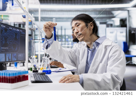 Clinical laboratory technologist investigates chemical sample properties using test tube in laboratory. Asian research facility professional holds vial containing new compound, doing pharmaceutical RD 132421461