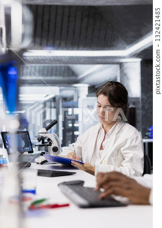 Scientist records observations from laboratory experiment for research documentation and scientific publication. Woman in lab doing data logging, taking notes, preparing clinical reports Scientist records observations from laboratory experiment for research documentation and scientific publication. Woman in lab doing data logging, taking notes, preparing clinical reports 132421485