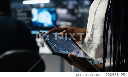 Close up of data center engineer using tablet to review code for automation scripts. Server farm system administrator using device, monitoring error logs for debugging processes, camera A Close up of data center engineer using tablet to review code for automation scripts. Server farm system administrator using device, monitoring error logs for debugging processes, camera A 132421495