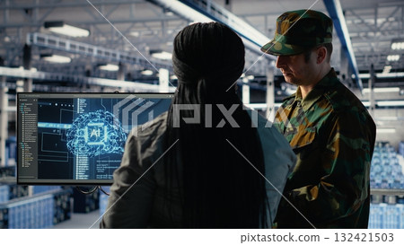 Military staff in server room uses AI tools to help manage computer systems. Army team wearing uniform reviews information using artificial intelligence programs in server farm, camera B Military staff in server room uses AI tools to help manage computer systems. Army team wearing uniform reviews information using artificial intelligence programs in server farm, camera B 132421503