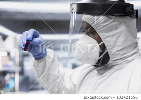 Black scientist in biocontainment lab conduct experiments on viral pathogens, treating a patient under isolation to develop immunization and pharmaceutical cures for epidemic infections. Black scientist in biocontainment lab conduct experiments on viral pathogens, treating a patient under isolation to develop immunization and pharmaceutical cures for epidemic infections. 132421556