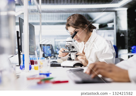 Cytotechnologist adjusting microscope, zooming on cellular structures in lab workspace. Molecular biologist observes specimens through magnification tool at laboratory bench workstation Cytotechnologist adjusting microscope, zooming on cellular structures in lab workspace. Molecular biologist observes specimens through magnification tool at laboratory bench workstation 132421582