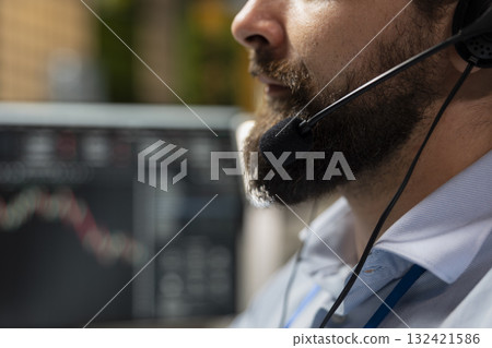 Close up of stockbroker in office speaking in audio headset mic, working with clients to develop investing strategies. Consultant chatting with customers, recommending stock exchange recommendations Close up of stockbroker in office speaking in audio headset mic, working with clients to develop investing strategies. Consultant chatting with customers, recommending stock exchange recommendations 132421586
