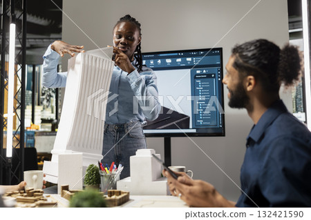 African american design engineer discuss measurements on 3D models and construction blueprints to respect zoning regulations. Strategic redevelopment project master plan for urban growth. 132421590