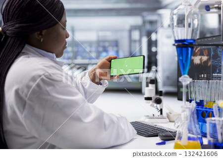 Black expert using chroma key screen for laboratory study on smartphone, works with experiment data for molecular science. Advanced research, pharmacology and biotechnology discovery. 132421606