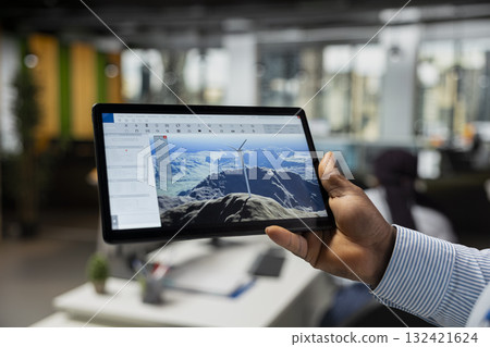 Close up of CAD engineer using tablet app in office to upgrade turbine, boosting power output, reducing carbon footprint. Worker using digital device to review windmill data to optimize clean energy 132421624