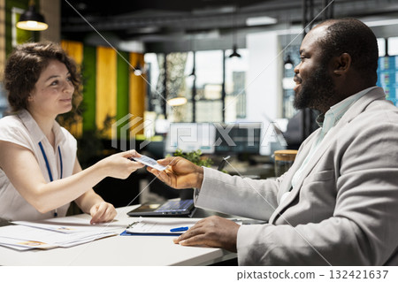 Interviewer handing workplace badge to new hire after the recruiting process, completing registration with ID confirmation on credentials for the role within the corporate office system. Interviewer handing workplace badge to new hire after the recruiting process, completing registration with ID confirmation on credentials for the role within the corporate office system. 132421637