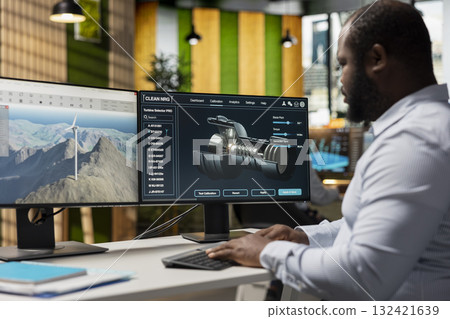 Technician in office analyzes wind turbine component to improve alternative energy efficiency. African american man uses CAD software to refine turbine part design, boosting clean energy output 132421639
