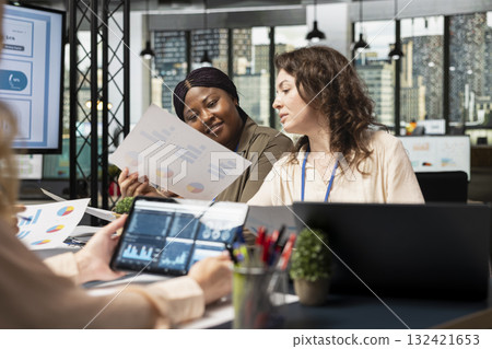 Group of business associates meeting in boardroom to align performance goals with project indicators, surrounded by reports and digital tools. Ambitious team showcasing collective success. 132421653