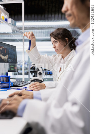 Clinical microbiologist in research facility using colorful chemical solutions in glassware. Clinical laboratory technologist looking at reagent vial ready to be used for experimental analysis 132421692