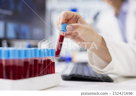 Close up of chemical engineer using laboratory glassware filled with red indicator solution at workstation in research facility. Lab specialist picking vial with chemical fluid used for experiments 132421696