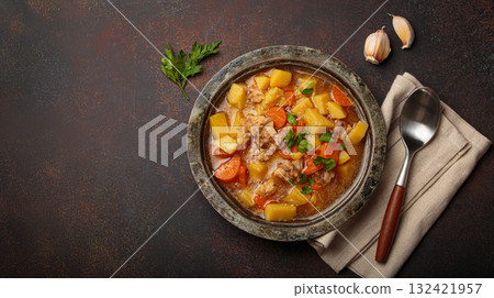 Chicken stew or soup with potatoes and carrots served in rustic bowl with spoon top view on dark brown concrete background, space for text 132421957