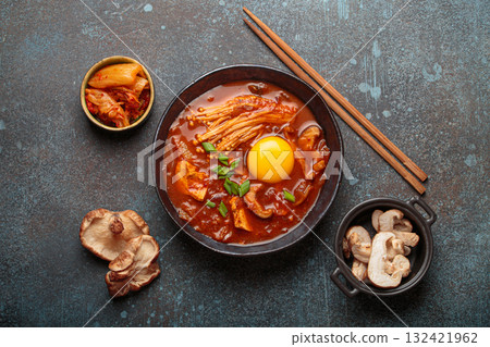 Traditional Korean kimchi jjigae hot soup or stew with egg yolk in black rustic bowl on dark background top view 132421962