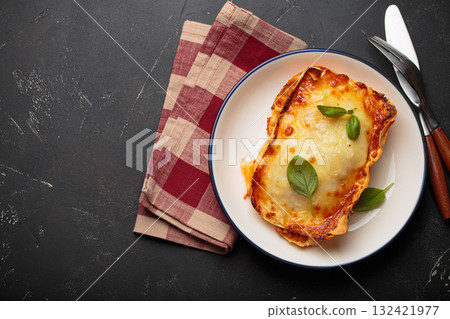 Traditional Italian lasagna on plate with basil garnish on rustic black background top view, space for text 132421977