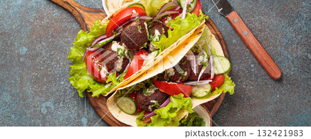 Falafel tacos with fresh vegetables and creamy tahini sauce served with hummus 132421983