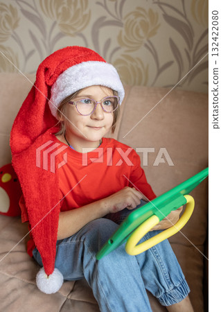 A girl in a Santa Claus hat opens a gift. It's Christmas time. A girl in a Santa Claus hat opens a gift. It's Christmas time. 132422080