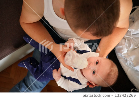 Young man feeding milk his baby boy son from bottle, view from above Young man feeding milk his baby boy son from bottle, view from above 132422269