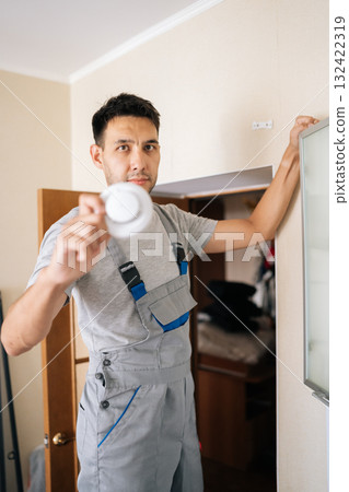 Vertical portrait of skilled electrician holding smoke detector while installing in residential building, prioritizing fire safety and ensuring protection for all occupants within home, looking camera Vertical portrait of skilled electrician holding smoke detector while installing in residential building, prioritizing fire safety and ensuring protection for all occupants within home, looking camera 132422319