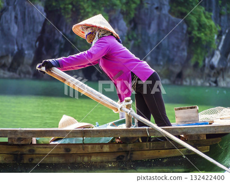 Rower in purple ao dai dress and conical hat paddling wooden sampan boat, Ha Long Bay, Vietnam 132422400