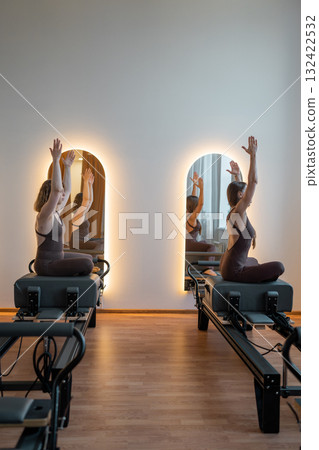 Two women in sunrise stretch with awareness, women reach and move in sunrise reformer flow Two women in sunrise stretch with awareness, women reach and move in sunrise reformer flow 132422532