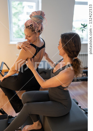 Pilates instructor adjusts posture, instructor meticulously corrects shoulder posture during session Pilates instructor adjusts posture, instructor meticulously corrects shoulder posture during session 132422533
