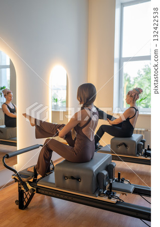 Group of caucasian women exercising with trainer on pilates reformers in a bright studio. Their workout focuses on core strength and flexibility in a modern fitness environment 132422538