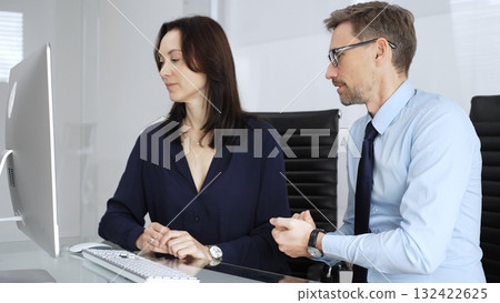 Businessman and business woman colleagues collaborating on computing project in office, discussing data, sharing ideas, and developing solutions, fostering teamwork and professional partnership 132422625